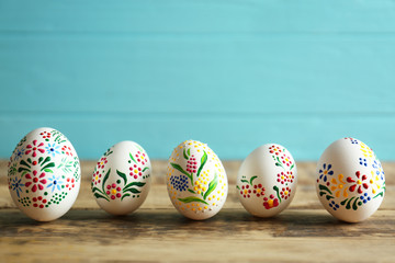 Colourful Easter eggs with floral ornament in a row on wooden table and blue background, closeup