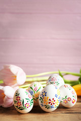 Fototapeta na wymiar Beautiful Easter eggs and flowers on wooden table and pink background, closeup