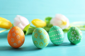 Beautiful Easter eggs and flowers on blue wooden background, closeup