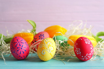 Beautiful Easter eggs and flowers on blue wooden table, closeup