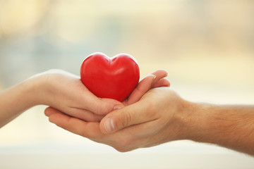 Naklejka na ściany i meble Male and female hands holding small red heart on blurred background