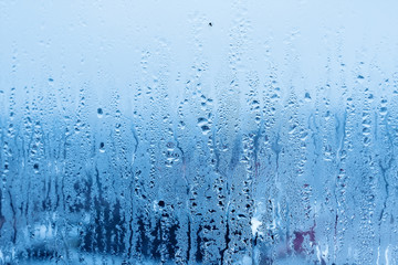 Window glass with condensation, strong, high humidity in the room, large water droplets flow down the window, cold tone, natural water drops on window glass