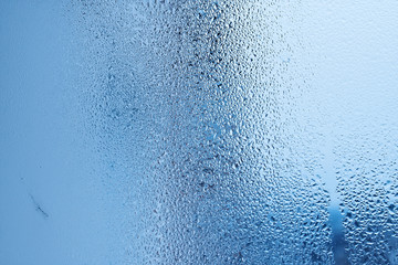 Window glass with condensation, strong, high humidity in the room, large water droplets flow down the window, cold tone, natural water drops on window glass