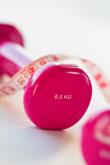 Pink fitness dumbbell with centimeter ribbon on bright shiny bac