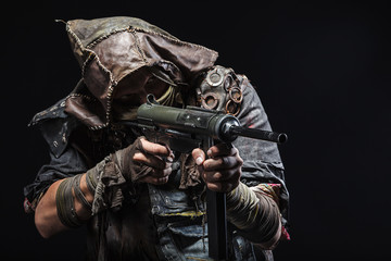 Nuclear post apocalypse life after doomsday concept. Grimy survivor with homemade weapons aiming a gun. Studio closeup portrait on black background