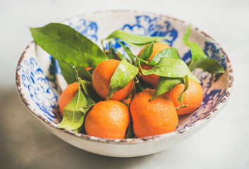 Freshly picked wet ripe mandarines with leaves in oriental white and blue plate over light grey background, selective focus