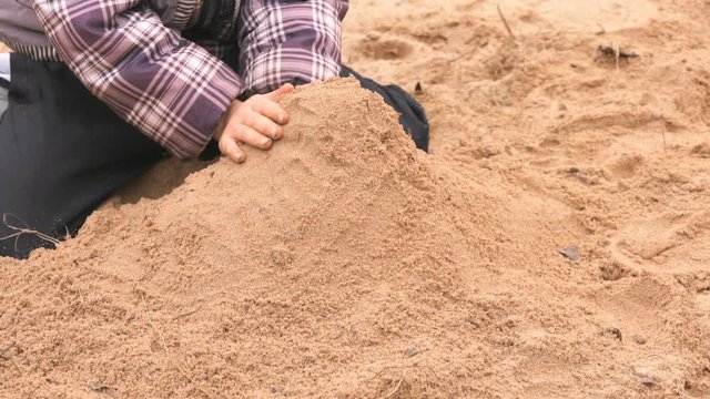 Hands of little kid in checkered jacket playing with sand and learning how to make shapes in outdoor sandbox. Close-up