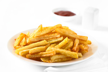 Fresh homemade crispy French fries on plate with a small bowl of ketchup and salt shaker in the back, photographed with natural light (Selective Focus, Focus in the middle of the image)