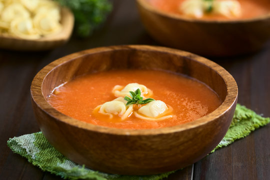 Homemade fresh cream of tomato soup with tortellini garnished with fresh oregano, photographed with natural light (Selective Focus, Focus on the front of the oregano on the soup)