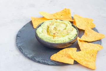 Healthy avocado hummus sprinkled with olive oil, paprika and sesame, served with nachos, horizontal