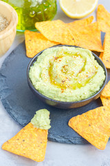 Healthy avocado hummus sprinkled with olive oil, paprika and sesame, served with nachos, vertical