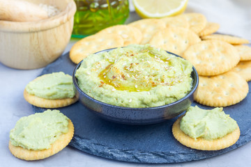 Healthy avocado hummus sprinkled with olive oil, paprika and sesame, served with crackers, horizontal