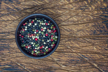 Four different kinds of peppercorns in clay bowl on wooden background, copy space, top view