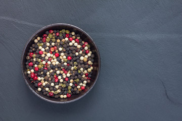 Four different kinds of peppercorns in clay bowl on stone background, copy space, top view