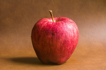 red apple with drop of water on skin put on brown background. Healthy fruit