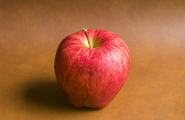 red apple with drop of water on skin put on brown background. Healthy fruit