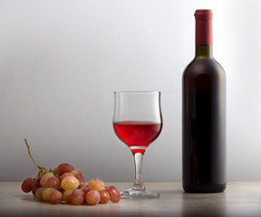Красное вино в бокале,гроздь винограда и бутылка вина на столе.