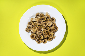 Вяленые (сушёные) ломтики бананов в тарелке на жёлтом фоне