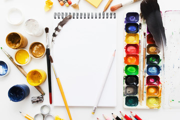 Naklejka premium Creative artist workplace flat lay, mockup. top view on table with blank sketchbook, pencils, paintbrushes and dye palettes. Art, workshop, painting, drawing, craft, creativity concept