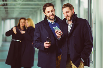 Two businessman holding smart phone in lobby with colleagues at background