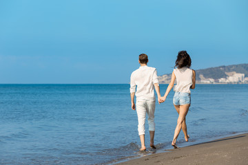 Couple walking on beach. Young happy interracial couple walking on beach smiling holding around each other.
