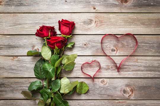 bouquet of red roses on wood background with hearts from ribbon.