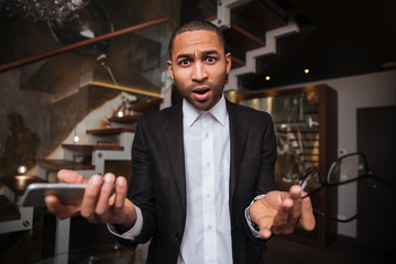 Displeased african man with phone in hotel