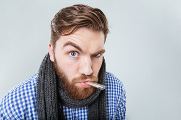 Amusing bearded man in scarf holding thermometer at his mouth