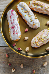 Vanilla eclairs with icing, rose petals and pistachios.