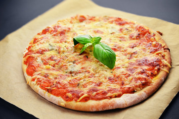 Pizza with cheeses and basil on black table.