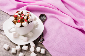 Hot chocolate in white cup with marshmallow and sweet hearts on the wooden table. Copy space