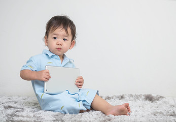 Closeup cute asian kid sitting with tablet on his hand at home on gray carpet and cement wall textured background with copy space