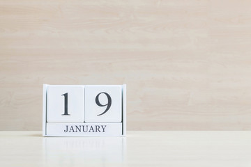 Closeup surface white wooden calendar with black 19 january word on blurred brown wood desk and wood wall textured background with copy space , selective focus at the calendar