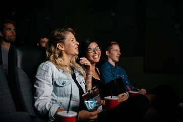 Happy young people watching movie in cinema - obrazy, fototapety, plakaty