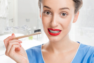 Portrait of confused woman with tooth braces holding a toothbrush at the bathroom. Woman worried about tooth cleaning with braces
