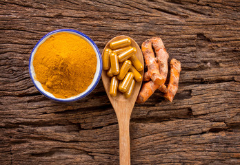 the turmeric powder , capsule and roots curcumin on wooden plate