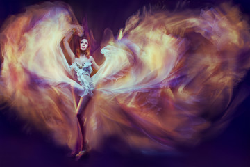 Woman dancing waving fantasy flame dress, flying fabric dance as fire in dark 