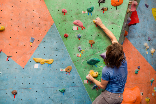 young man climbing artificial boulder indoors, modern sport concept