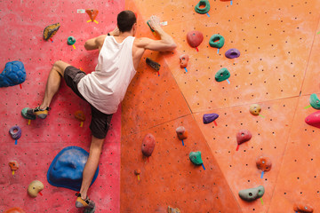 Man climber on artificial climbing wall in bouldering gym - obrazy, fototapety, plakaty