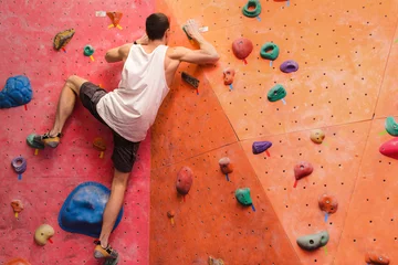Gordijnen Man climber on artificial climbing wall in bouldering gym © EdNurg