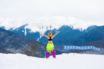 Young active girl stands on the top of mountain with ski suit taken off and hands wide open enjoy beautiful view