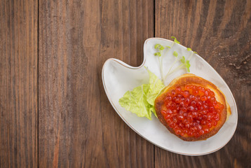 healthy appetizer : sandwich with red caviar on white china plate. Wooden background. Top view. Close-up