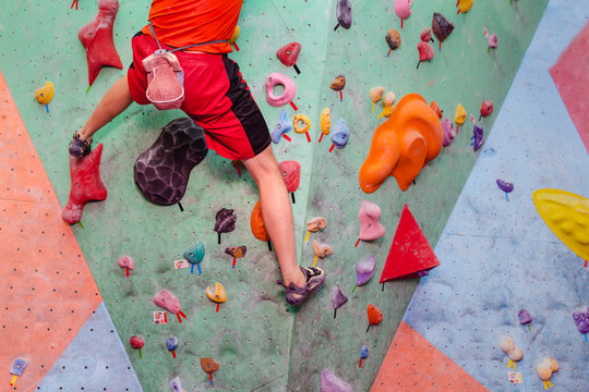 Man climbing artificial boulders in gym, close-up view of legs with special shoes