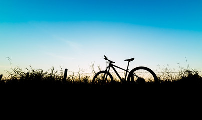 Silhouette mountain bicycle and fields on blue sky