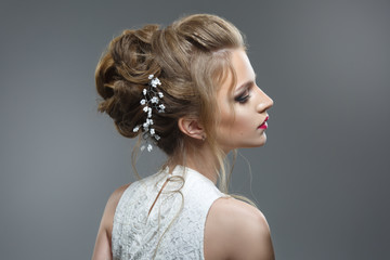 Elegant bride with a beautiful hairstyle and bright make-up isolated on a gray background.