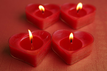 Fototapeta na wymiar Heart shape candles. Four red candles burning.