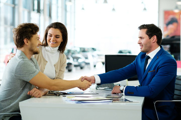 Salesman and customer shaking hands congratulating each other at the dealership showroom