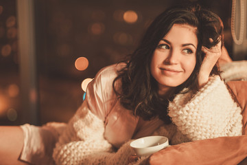 Portrait of beautiful young woman with cup of hot drink in cozy home interior