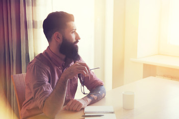 Bearded man with glasses writing with pen in notebook
