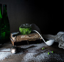 rustic still life, vintage. green peas, old books, flour on a wooden table. dark background